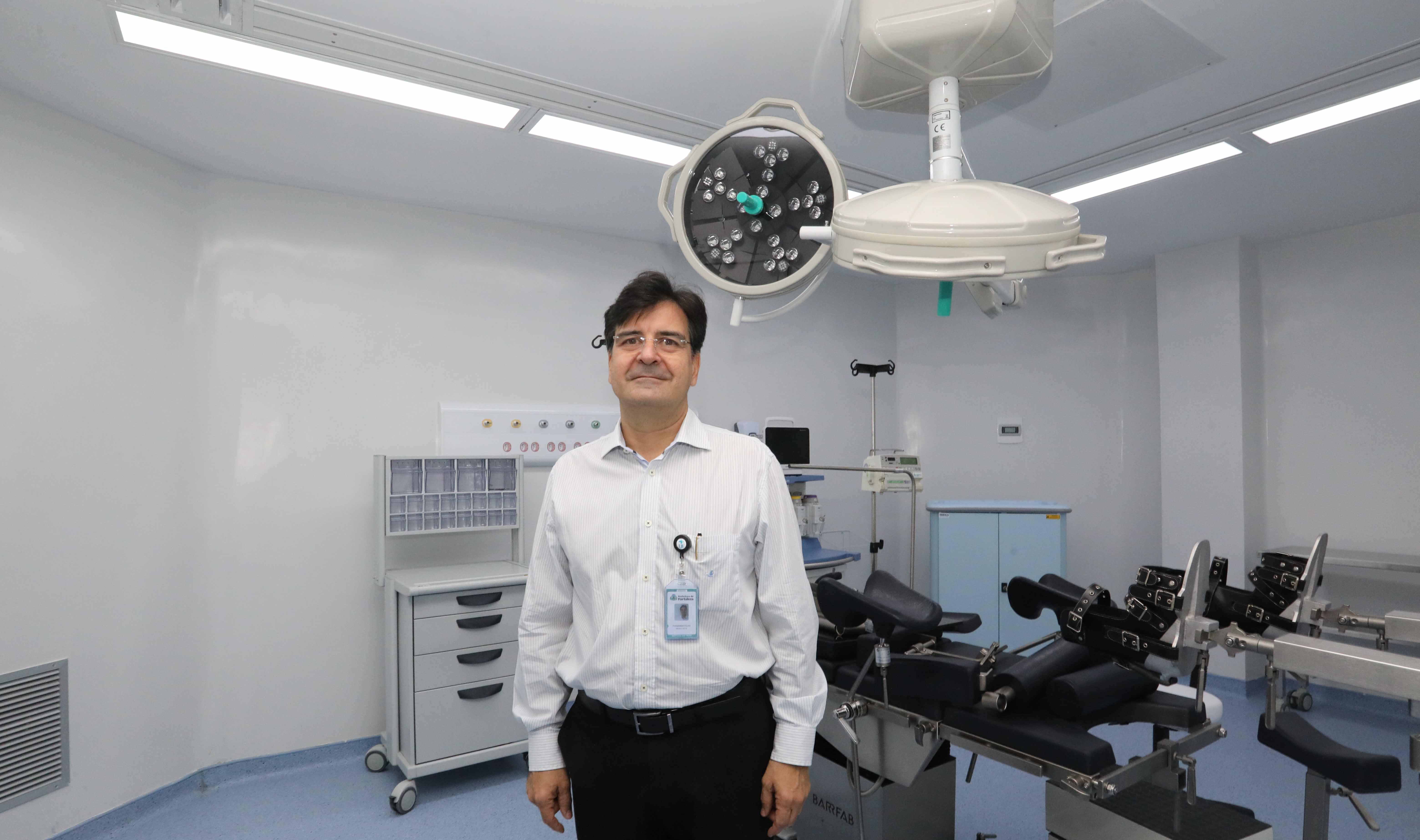 senhor posando para a foto em sala de cirurgia com maca e equipamentos ao fundo